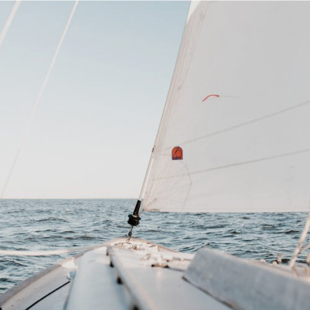 View from the deck of a sailboat with white sails against the open sea.