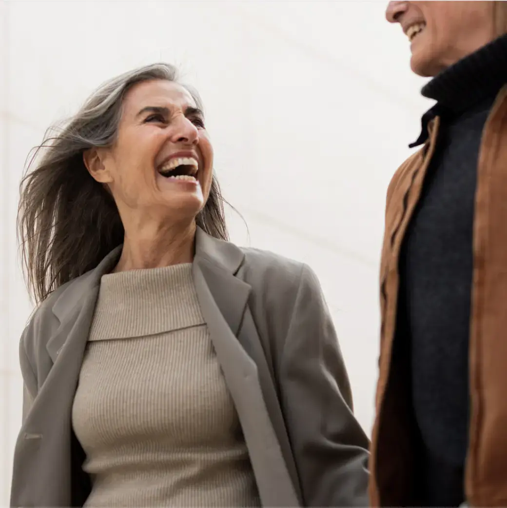 Smiling couple walking outdoors, the woman laughing while holding the man’s arm.