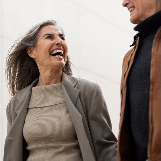 Smiling couple walking outdoors, the woman laughing while holding the man’s arm.