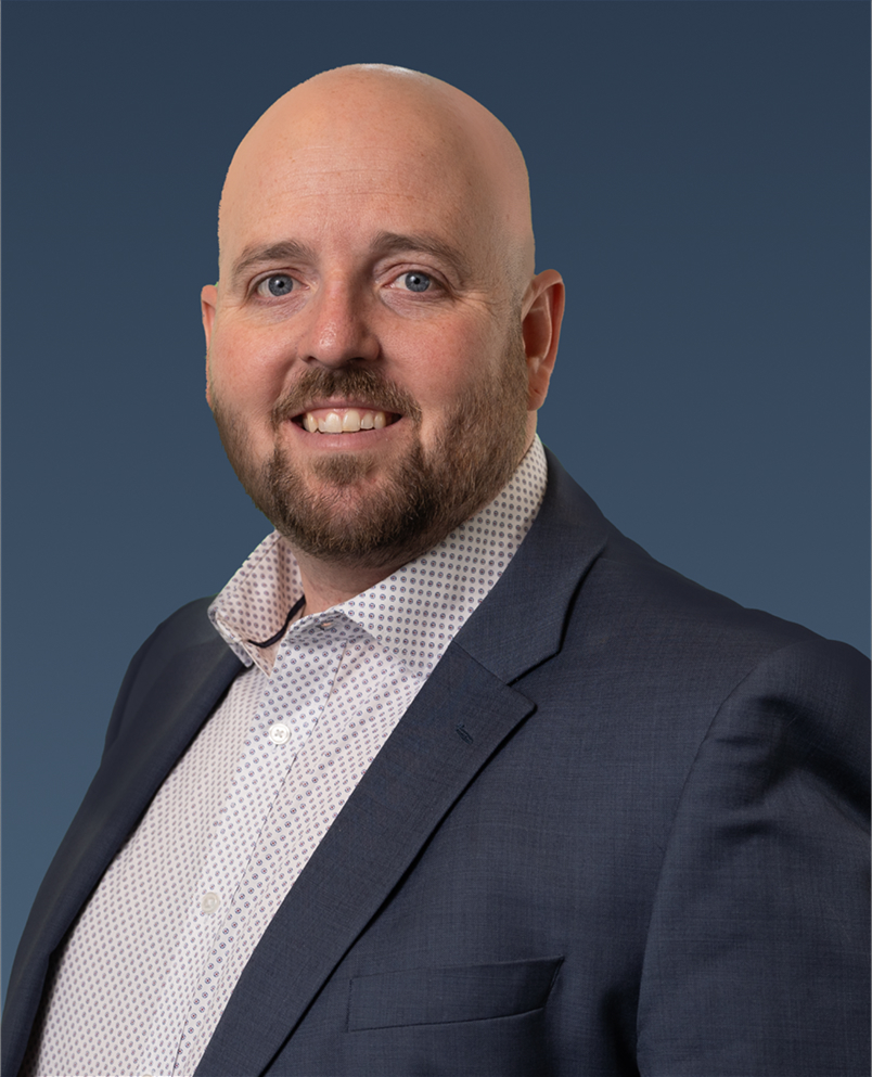 Professional portrait of a blonde man wearing a black blazer and patterned scarf.