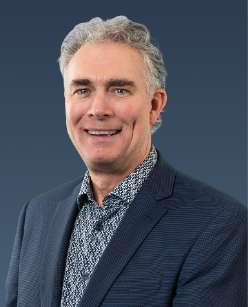 Professional portrait of a man with gray hair in a blazer and patterned shirt, looking forward.