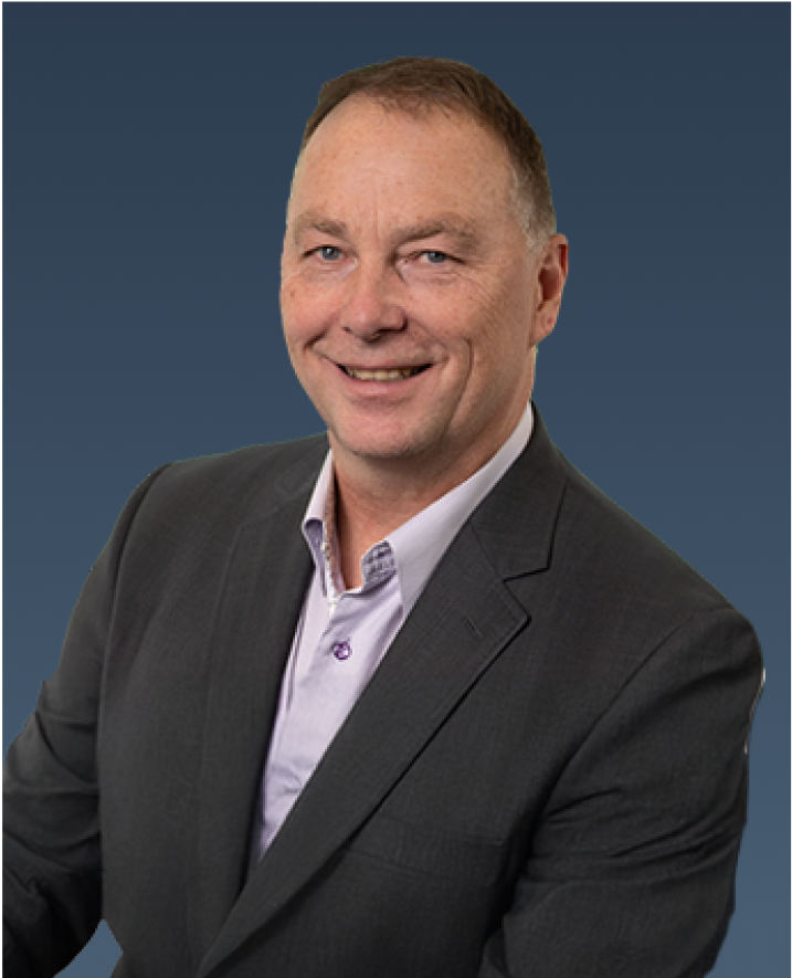 Professional portrait of a man in a dark suit and light shirt, smiling slightly against a blue background.