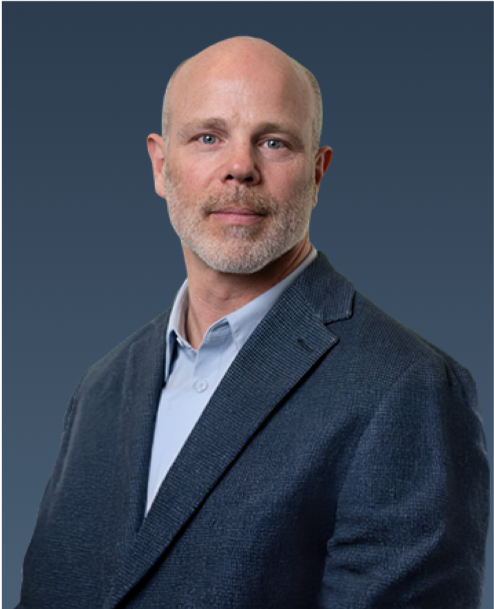 Professional portrait of a bald man with a trimmed beard, wearing a dark blazer over a light shirt.