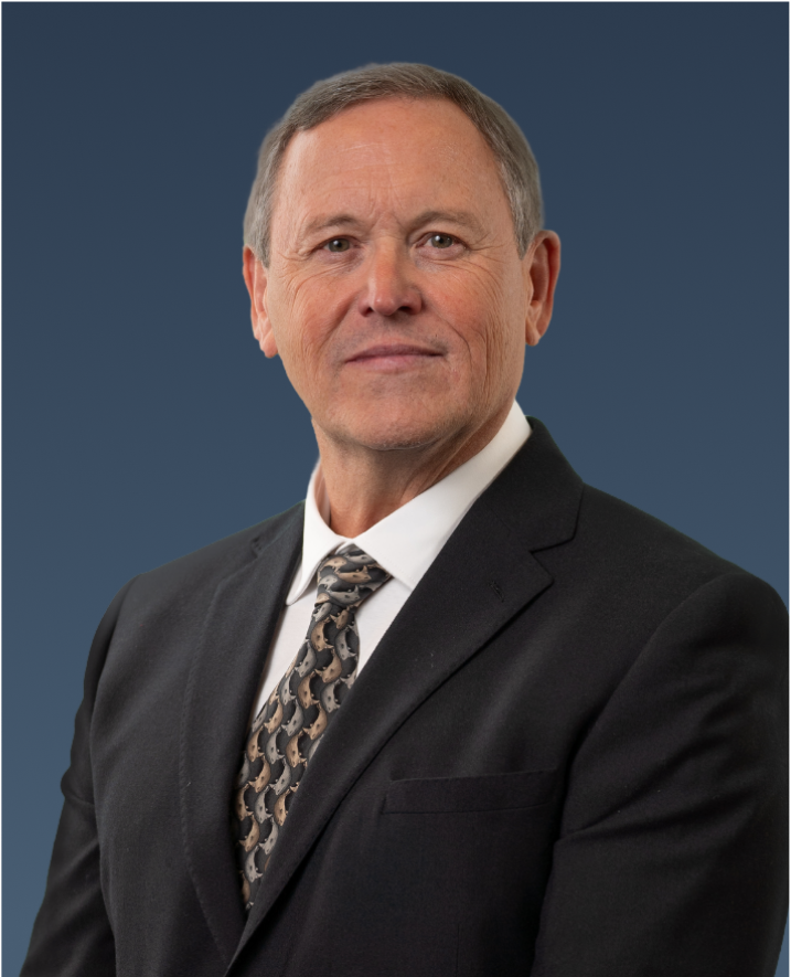 Professional portrait of a man in a black suit and patterned tie, with a neutral expression.